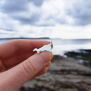 Kernow Cornwall map silver brooch pin, held against backdrop of Portscatho beach 