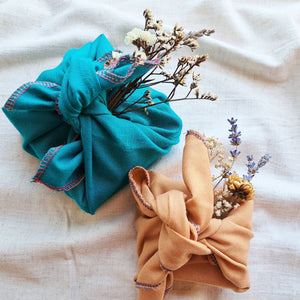 Turquoise and orange fabric gift wraps, tied in furoshiki style knot with dried flowers tucked inside