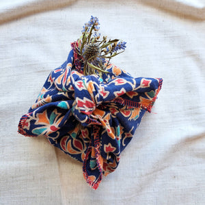 Blue, orange, red and green flower patterned fabric gift wrap with dried blue thistle and lavendar posy, tied in furoshiki knot