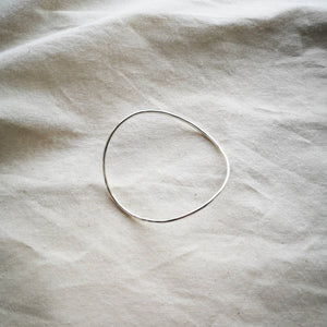 Minimalist curved silver bangle, on natural calico fabric 