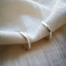 Load image into Gallery viewer, Front view of hammered textured silver hoop earrings on muslin fabric
