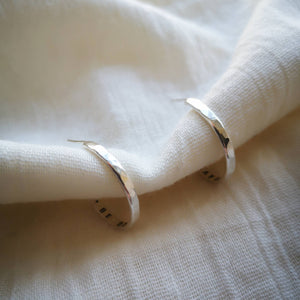 Front view of hammered textured silver hoop earrings on muslin fabric