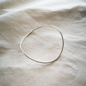 Sustainable recycled silver bangle, curved wavy shape, on plain natural cream fabric 