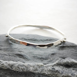 Handmade silver wave bangle closeup showing hammered faceted texture and silver balls on Cornish slate stone