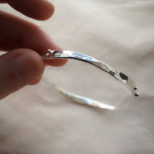 Load image into Gallery viewer, Fingertips holding textured recycled silver wave bangle to show hammered textured reflecting in light