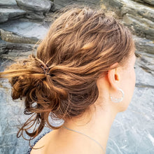 Load image into Gallery viewer, Cornish barrel wave sea themed earrings, recycled sustainable silver hoops worn by woman with brown hair on beach