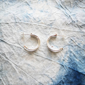 Sustainable recycled silver hoop earrings in style of crashing ocean waves, on blue and white fabric