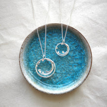 Load image into Gallery viewer, Two sizes of handmade silver wild wave pendants, inside ceramic blue glass trinket dish
