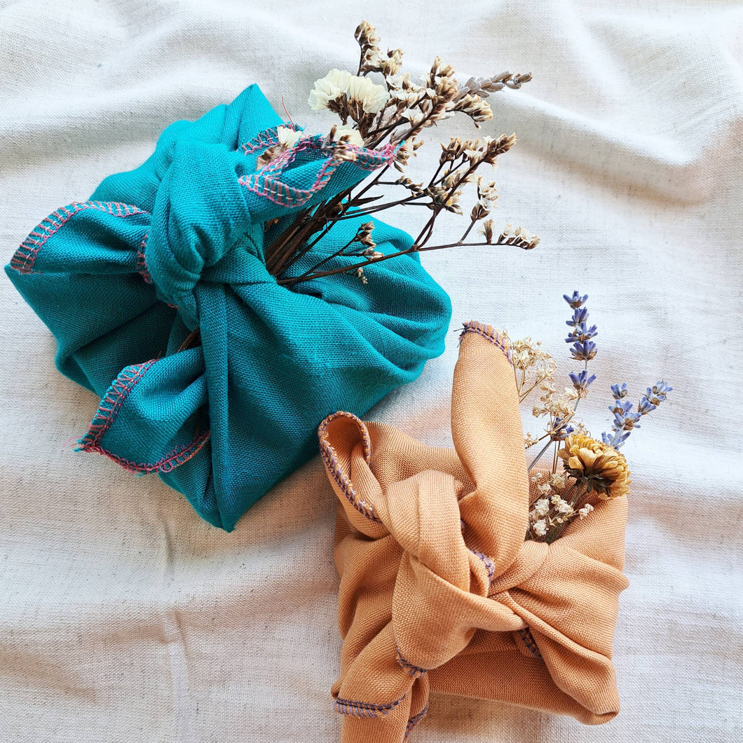 Sustainable fabric furoshiki gift wraps, one turquoise and one orange wrapped with dried flowers