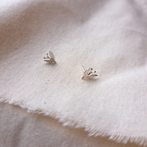 Silver leaf and berry stud earrings on plain natural calico fabric
