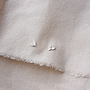 Silver leaf stud earrings on natural undyed cotton calico fabric