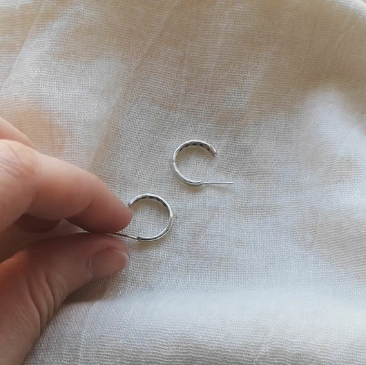 Fingers picking up mini silver hoops showing hidden message of 'hope' written inside