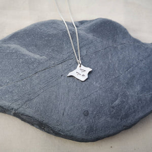 Silver Isle of Wight shaped necklace with three birds engraved, lying on a grey slate stone