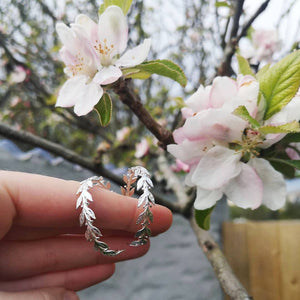 Silver leaves hoop earrings held next apple blossom tree