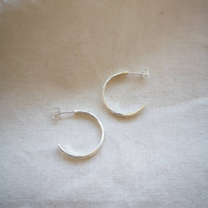 Side profile of textured simple silver hoop earrings on neutral background