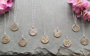 Selection of recycled silver antique-style love token coin necklaces on slate, including sunflower, arrows, whale & stars