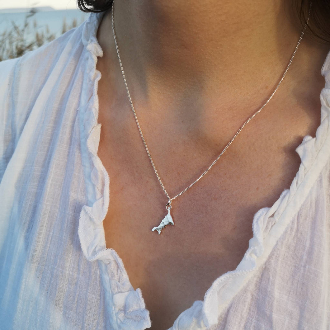 Mini Cornish map necklace, worn with minimal white shirt on Cornish cliff sea in background