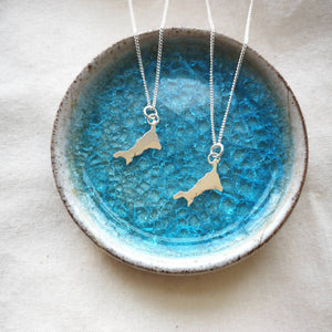Two mini silver Cornwall map necklaces on recycled silver chains lying in blue glass ceramic dish
