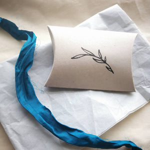 Sustainable packaging, recycled card pillow box with leaves stamped, white tissue paper and turquoise recycled sari ribbon
