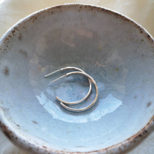 Side view of handmade sustainable silver hoops in a light blue glazed ceramic dish