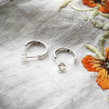 Load image into Gallery viewer, Handmade silver mini hoop earrings with secret hearts stamped inside, on fabric with orange flowers
