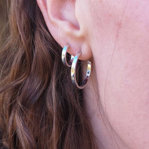 Hidden meaningful messages inside eco silver hoop earrings, two pairs worn by woman with brown hair, close up 