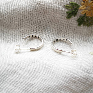 Mini silver hoop earrings with hope message inside, on fabric with embroidered yellow flower