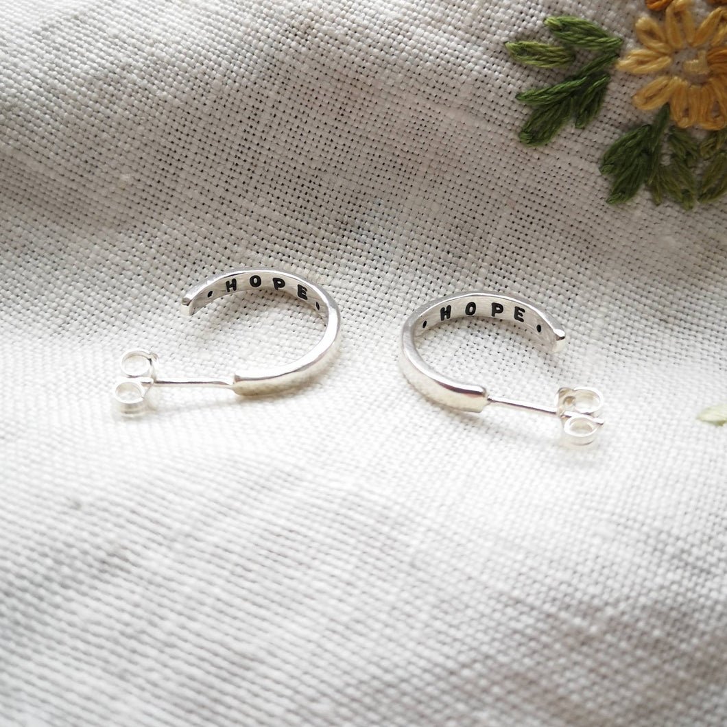 Mini silver hoop earrings with hope message inside, on fabric with embroidered yellow flower