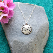 Load image into Gallery viewer, Personalised recycled silver love token coin necklace, engraved with infinity symbol, on stone background with pink flowers
