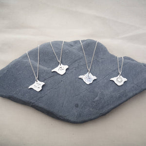 Isle of Wight silver necklaces displayed on grey stone, individual designs - birds, wave, textured and heart