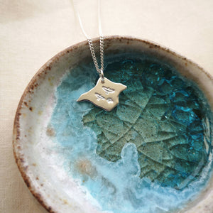 Silver Isle of Wight shaped necklace with three birds flying engraved, in blue and white glass dish