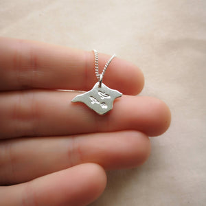 Hand holding silver Isle of Wight shaped necklace with three birds engraved on front
