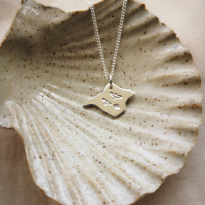 Three birds stamped on silver Isle of Wight shaped pendant, draped in a ceramic shell dish