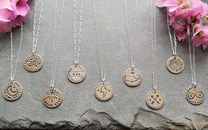 Selection of recycled silver antique-style love token coin necklaces on slate, including sunflower, arrows, whale & infinity 