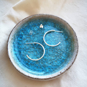 Handmade medium sized silver hoop earrings with scroll butterfly backs on blue glass and ceramic dish