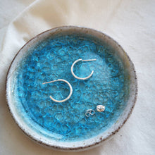 Load image into Gallery viewer, Small and simple silver hoops on blue ceramic and crackle glazed glass dish 
