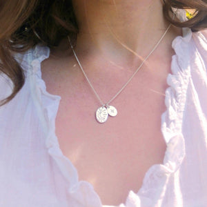 Close up of woman wearing two oval shaped reversible silver necklaces, one with moon one with star design