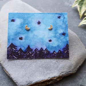 Half moon silver stud earrings on eco friendly backing card with a night forest and sky illustration in blue