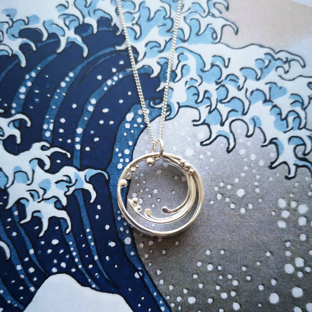 Recycled silver handmade wave pendant on background of The Great Wave Off Kanagawa ocean print