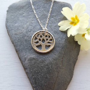 Recycled silver tree of life necklace, handmade with hidden message, on stone background with yellow primrose 