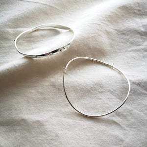 Two bangle on natural calico fabric, one slim curved ripple bangle, one chunkier wave bangle with silver balls