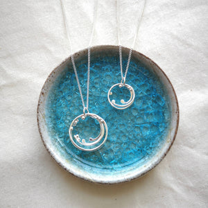 Two handmade recycled silver wave necklaces displayed in blue crackle glass ceramic dish